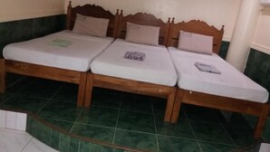 Een kamer met drie houten bedden, voorzien van witte matrassen en hoofdborden, een vloer met groene tegels en een witte muur met een witte airconditioning.