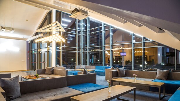 A modern lounge area with sofas, tables, and large windows offering views of the city. - Park Hotel Asarel (Panagyurishte)