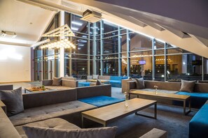 A modern lounge area with sofas, tables, and large windows offering views of the city. - Park Hotel Asarel (Panagyurishte)
