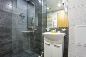 Un baño moderno con ducha acristalada, un lavabo blanco con artículos de aseo y un armario de madera.