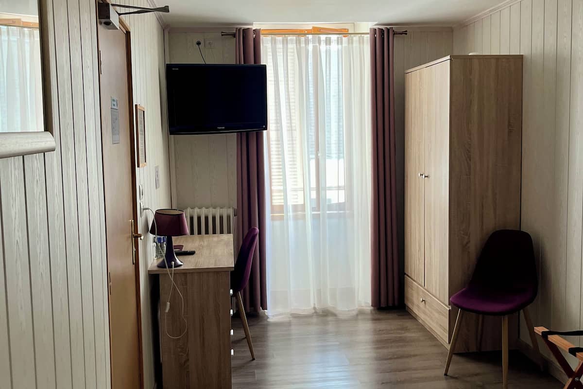 Una habitación de hotel con cama, escritorio con computadora, silla, armario y televisor.