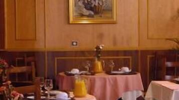 A dining area with tables set for breakfast, featuring pink tablecloths and a pitcher of orange juice.