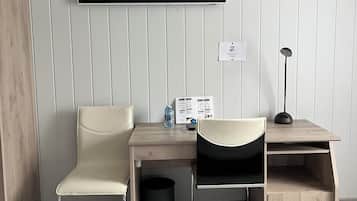 A modern hotel room with a desk, two chairs, a TV, a lamp, and a trash bin.