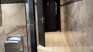 A hallway with marble walls, a hand sanitizer dispenser, and a door with a wheelchair accessibility sign. - Relais de la Poste (Pithiviers)