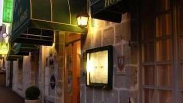 Fachada de hotel con un toldo verde, un letrero que dice "HOTEL" y dos plantas en macetas.