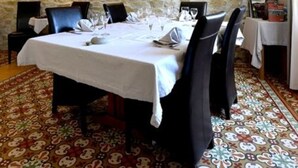 Een eetkamer met een stenen muur, een tafel gedekt voor zes personen, en een kamerbreed tapijt met dessin.
