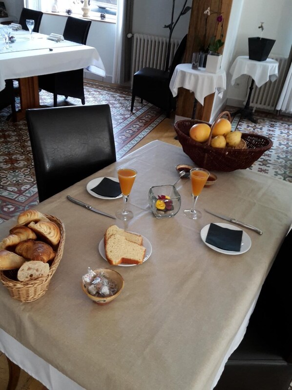 Une table dressée pour le repas, avec du pain, des croissants, un panier de fruits et des verres de jus d’orange.