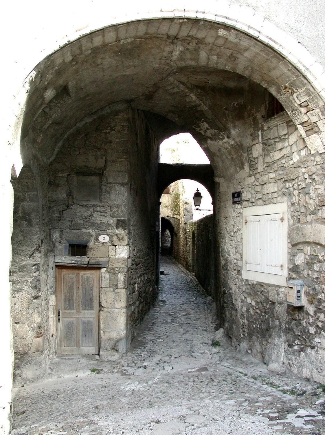 Un corredor de piedra con arco, una puerta de madera y una pizarra en la pared.