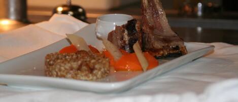 Un plato con un jarrete de cordero, zanahorias y un recipiente pequeño con salsa, posiblemente en un restaurante.