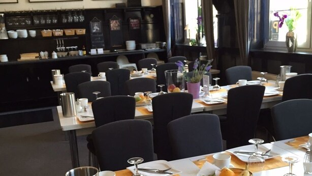 A dining area with tables set for service, a coffee station, and framed artwork on the wall.