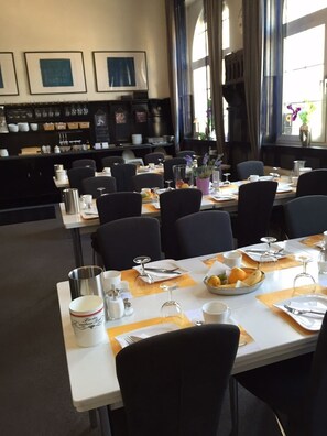 A dining area with tables set for service, a coffee station, and framed artwork on the wall.