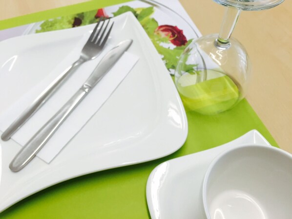 A dining setup with a white plate, a fork, a knife, a glass of water, and a green placemat.