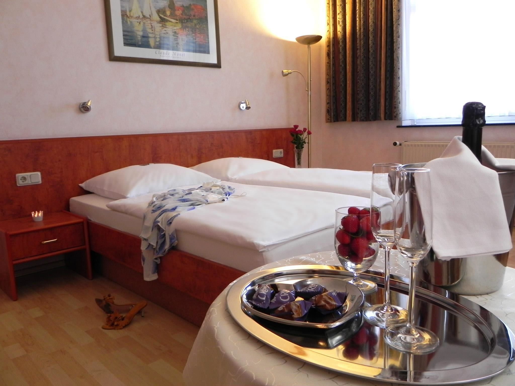 Een hotelkamer met twee bedden, een nachtkastje, een dienblad met snacks en een schilderij aan de muur.