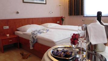 Een hotelkamer met twee bedden, een nachtkastje, een dienblad met snacks en een schilderij aan de muur.