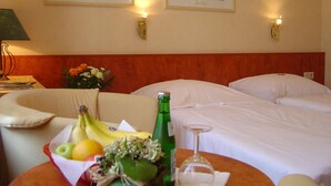 A hotel room with two beds, a table with fruit and a bottle, and two framed pictures on the wall.