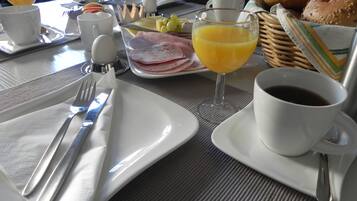 Une table de petit-déjeuner dressée avec des assiettes, des couverts, des verres de jus d’orange, une tasse de café et un panier de pain.