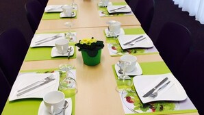 A conference room with a long table set for a meeting, equipped with chairs, plates, cutlery, and glassware.