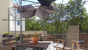 An outdoor patio with wooden tables and benches, surrounded by metal railings and potted plants.