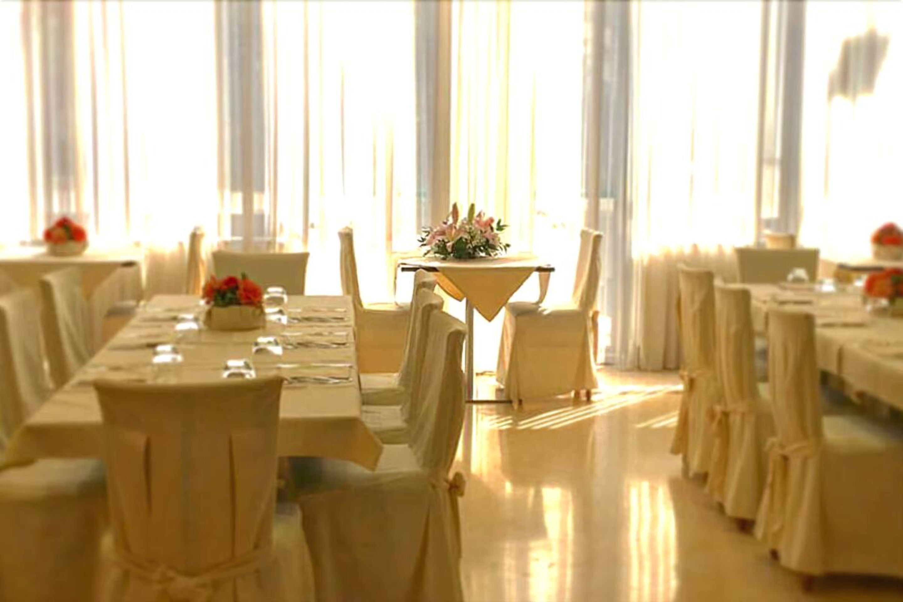 A banquet hall with multiple tables and chairs, arranged in rows.