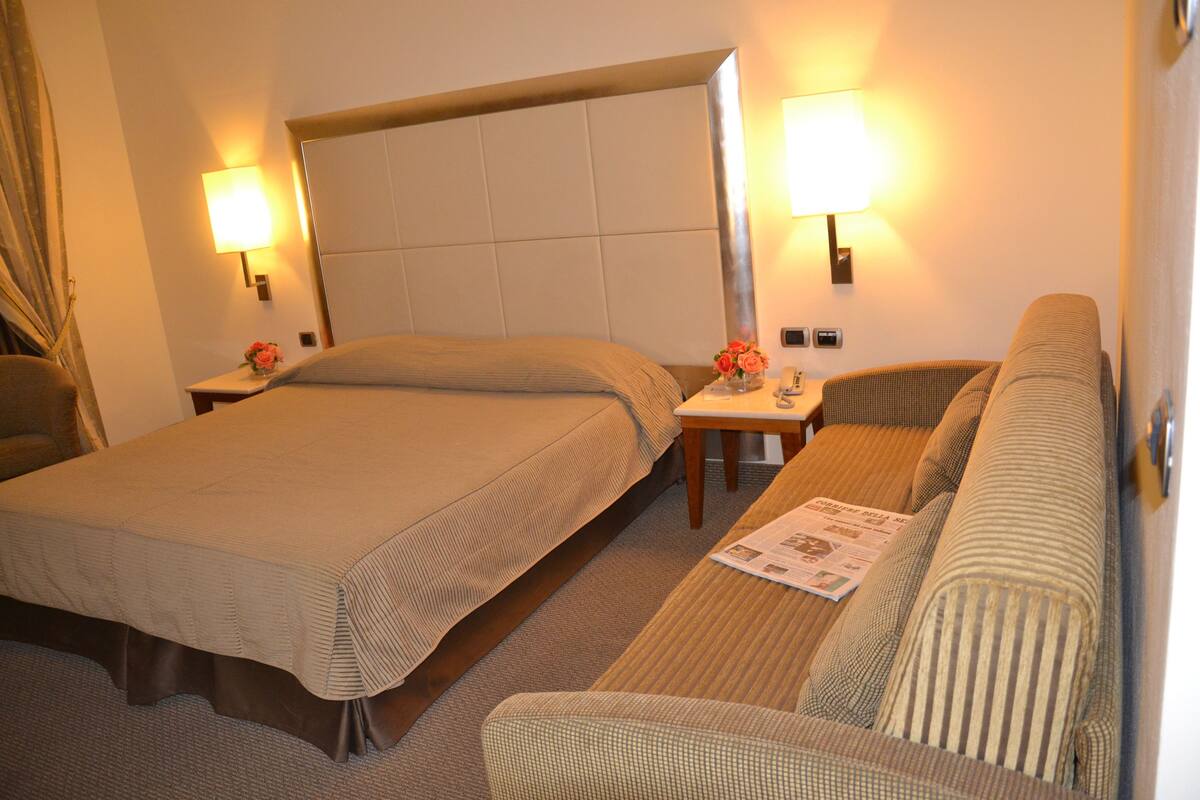 A hotel room with two beds, a sofa, and two bedside lamps.