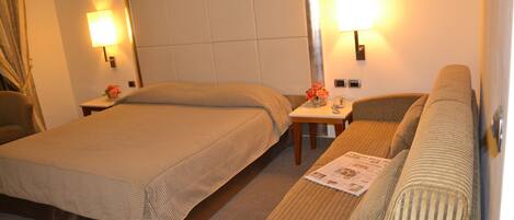 Ein Hotelzimmer mit zwei Betten, einem Sofa und zwei Nachttischlampen.