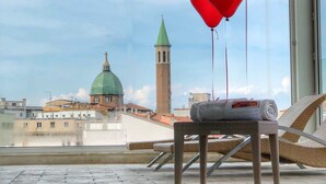 A balcony with a view of a church and tower, a chair, and red heart-shaped balloons. - Hotel Airone (Grosseto)