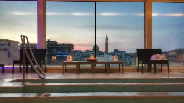 A room with a view of a cityscape, featuring a pool, a table with candles, and two chairs. - Hotel Airone (Grosseto)