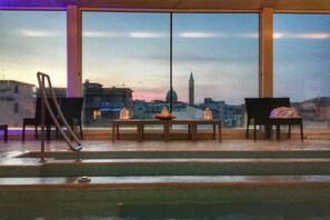 A room with a view of a cityscape, featuring a pool, a table with candles, and two chairs. - Hotel Airone (Grosseto)