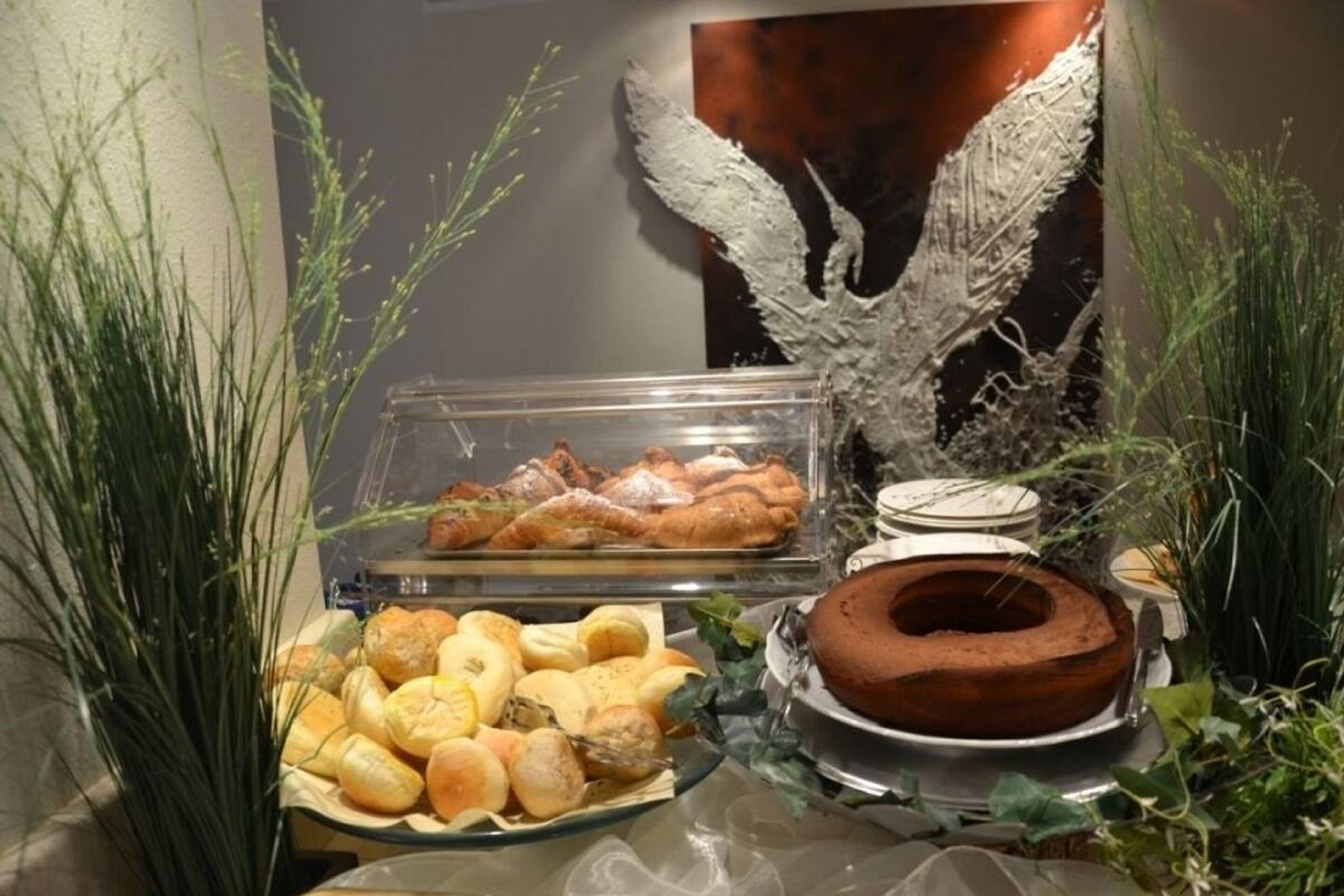 Un buffet proposant une variété de produits de boulangerie, notamment du pain et des viennoiseries, ainsi qu’un gâteau au chocolat.