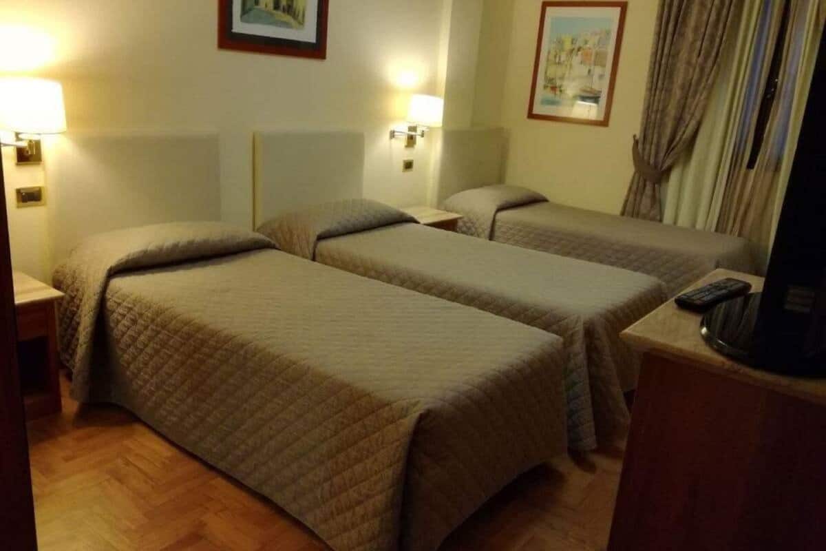 A hotel room with two single beds, bedside lamps, a television, and a wooden floor.