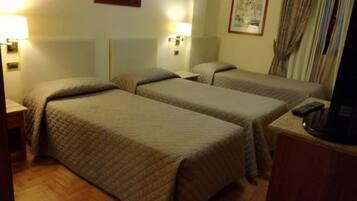 A hotel room with two single beds, bedside lamps, a television, and a wooden floor.