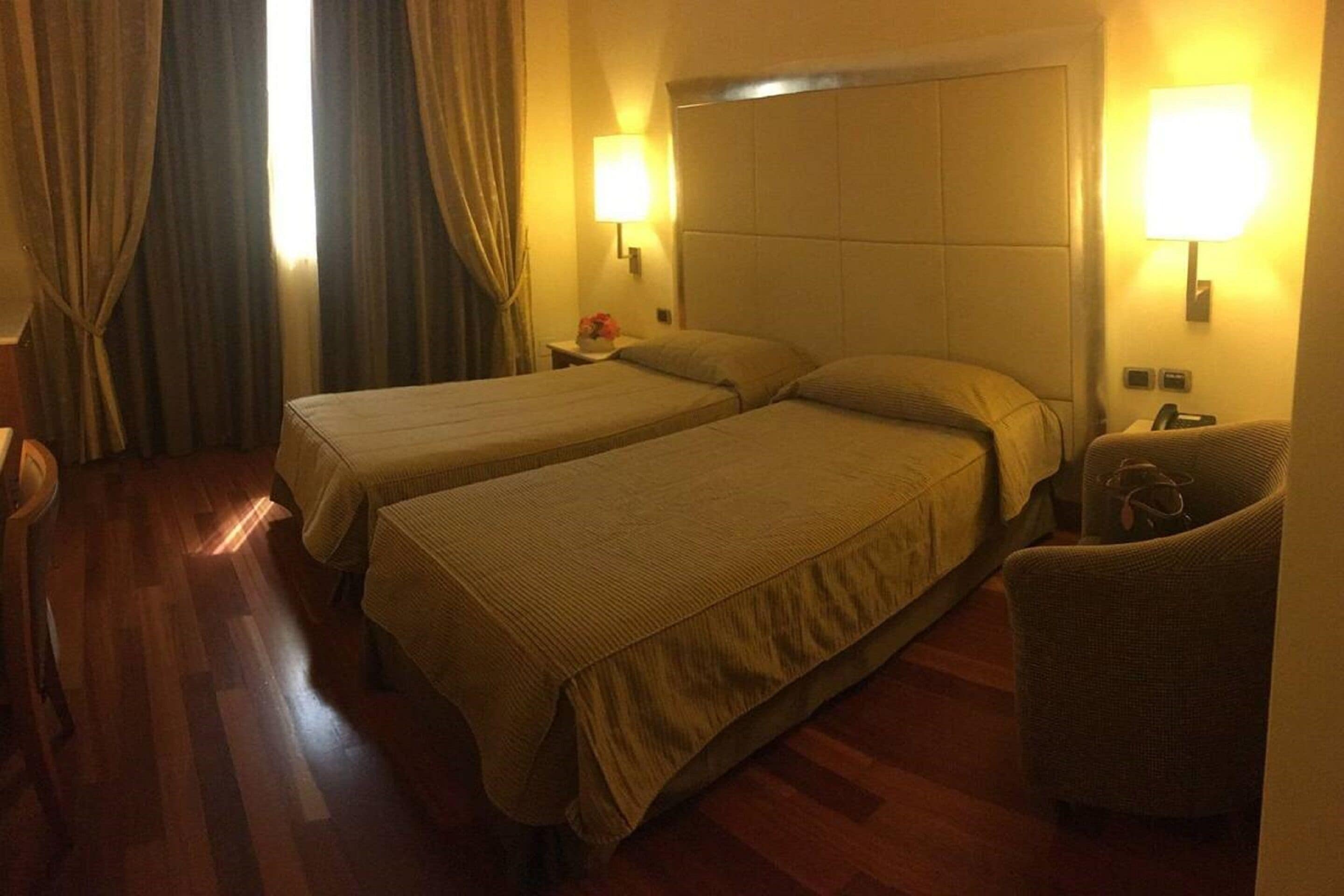 A hotel room with two beds, wooden flooring, and a chair.