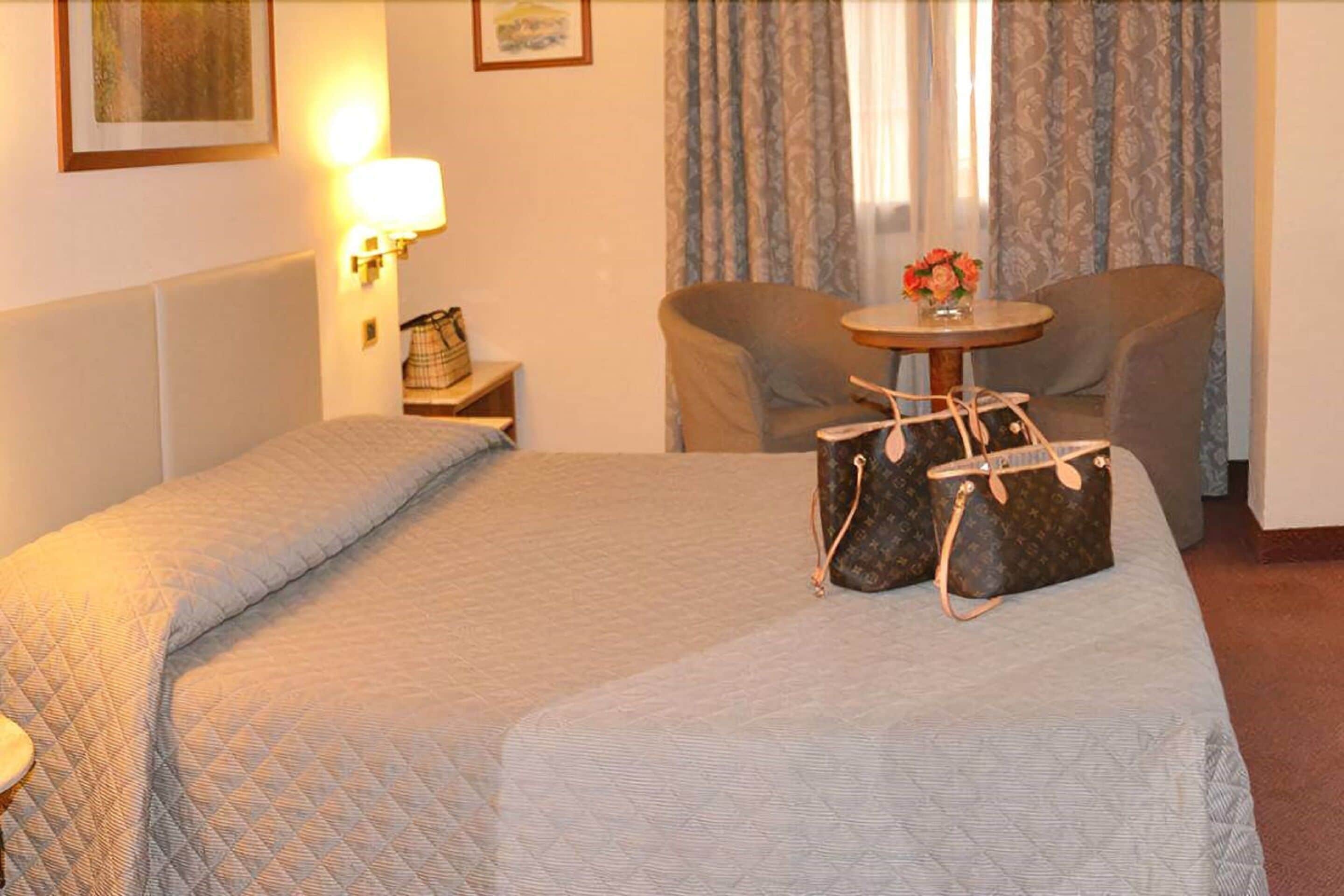 Una habitación de hotel con dos camas, una mesita con un florero y dos sillas.