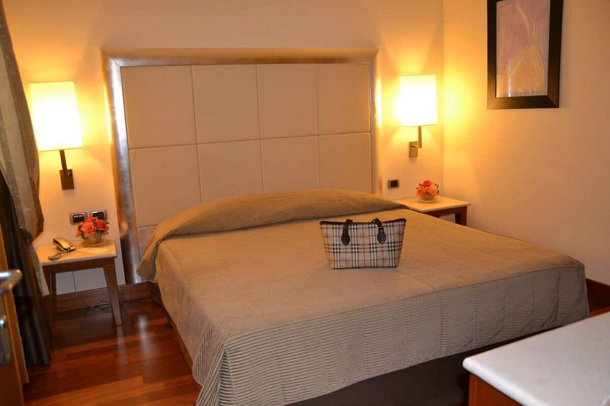 A hotel room with a large bed, two bedside tables, a nightstand, a lamp, and a framed picture on the wall.
