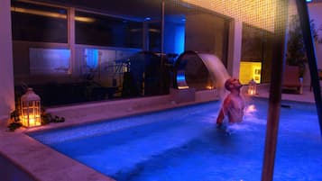 A swimming pool with a person in the water, surrounded by lounge chairs and a lantern.