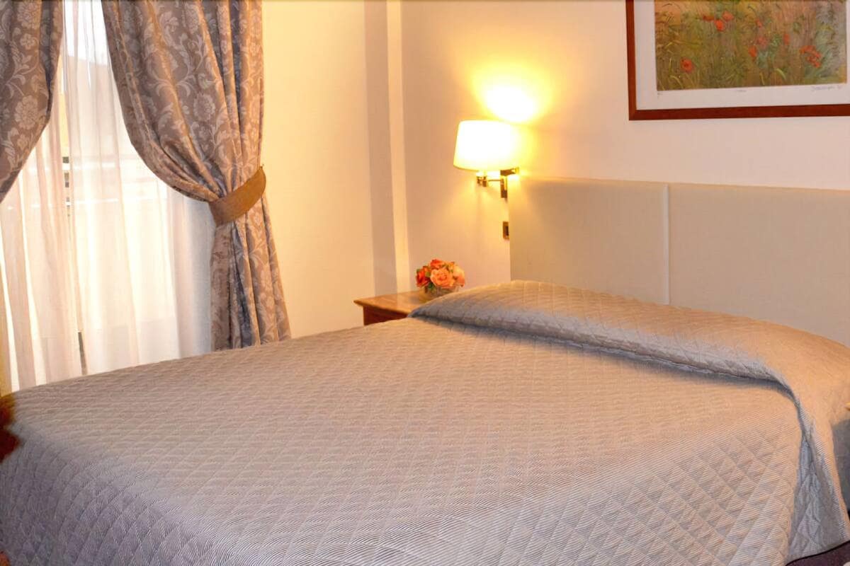 A neatly made bed with a quilted blanket, a bedside lamp, and a small vase with flowers on a nightstand.