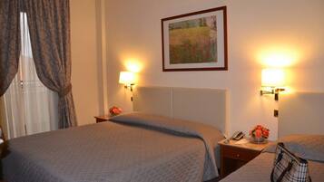 A hotel room with two beds, a nightstand with a lamp, a framed picture on the wall, and a window with curtains.