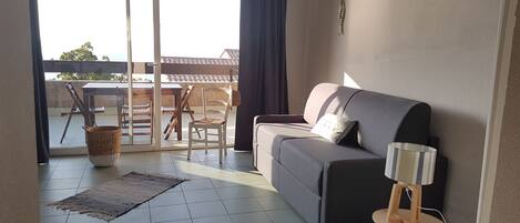 Un salón con sofá, una mesita, una lámpara y vistas al exterior.