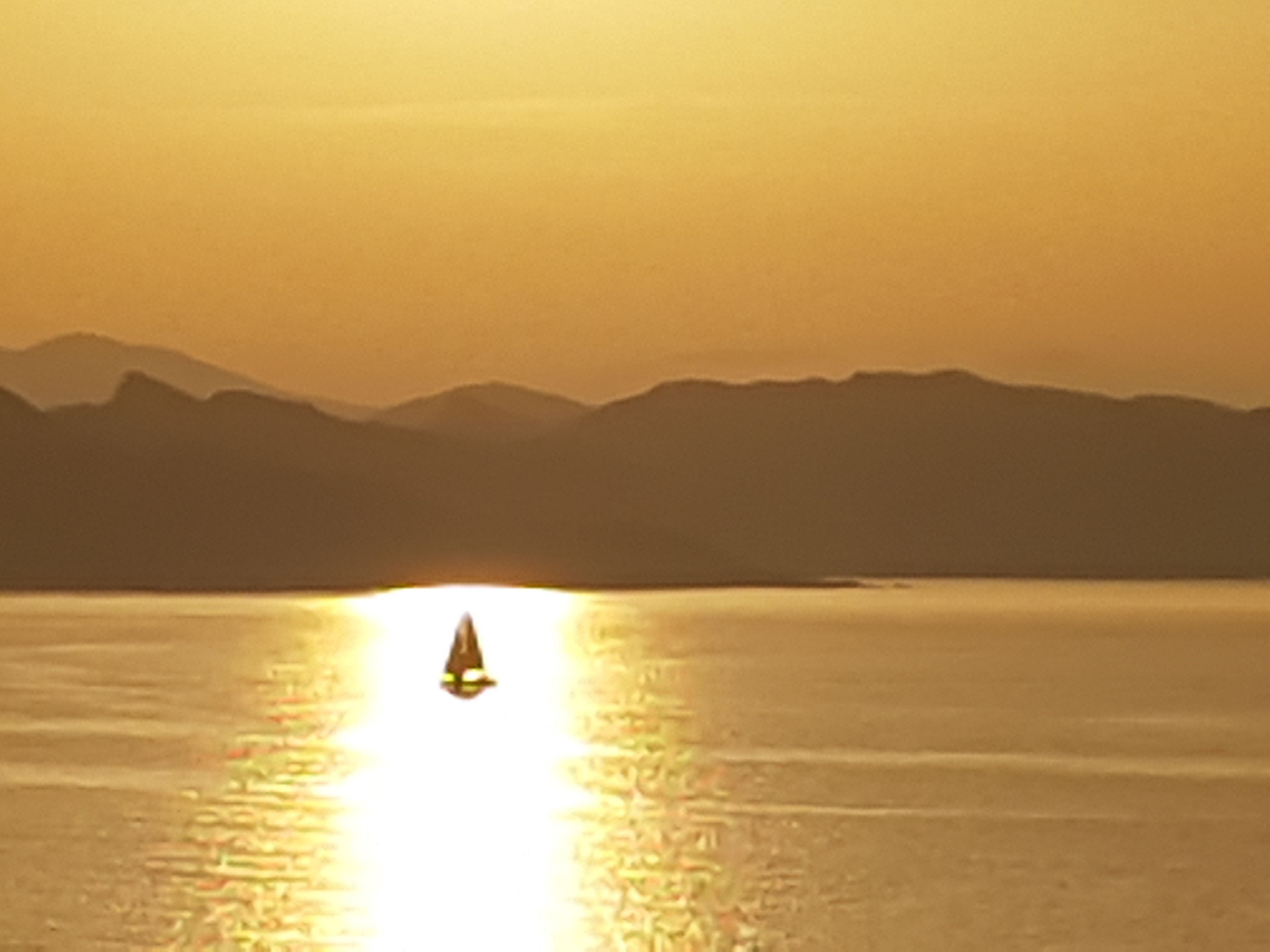 Un bateau sur une étendue d’eau calme, avec une chaîne de montagnes en arrière-plan.