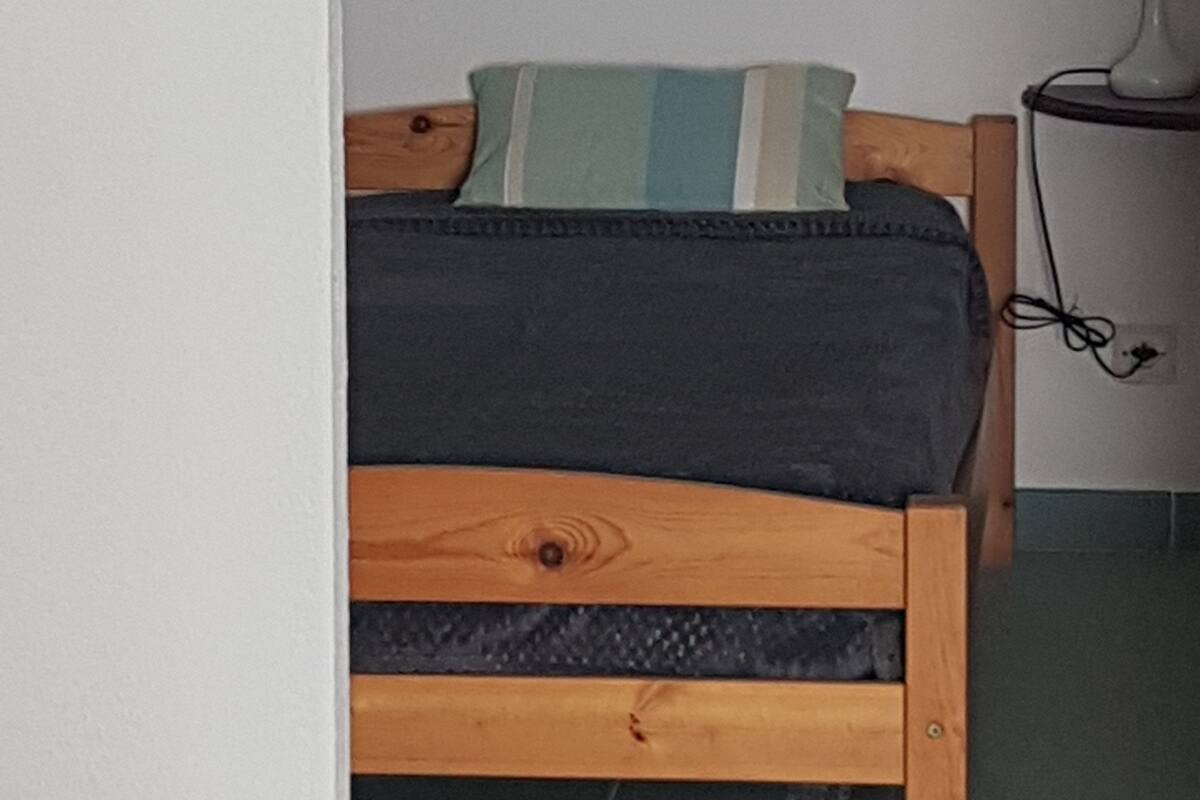 A bedroom with a wooden bed, a pillow, and a bedside table with a lamp.