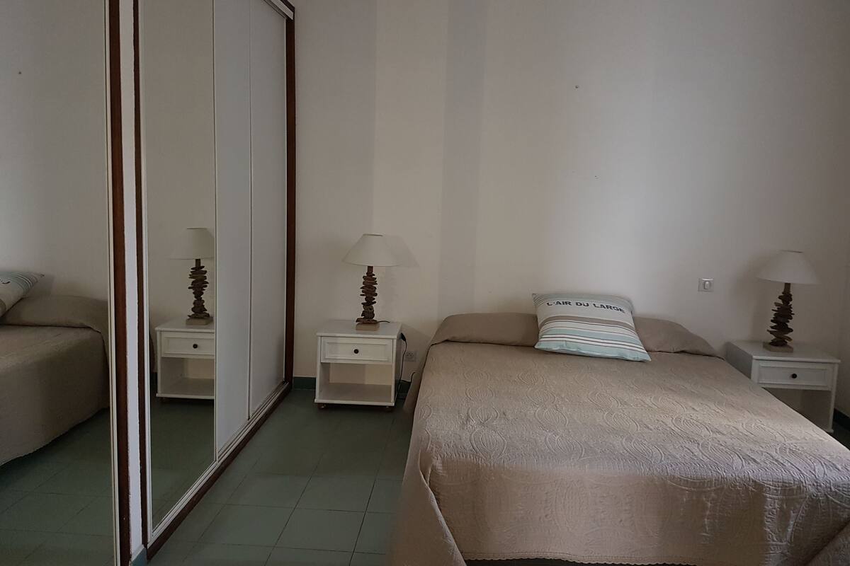 A bedroom with a bed, two bedside tables with lamps, a wardrobe, and a mirror.