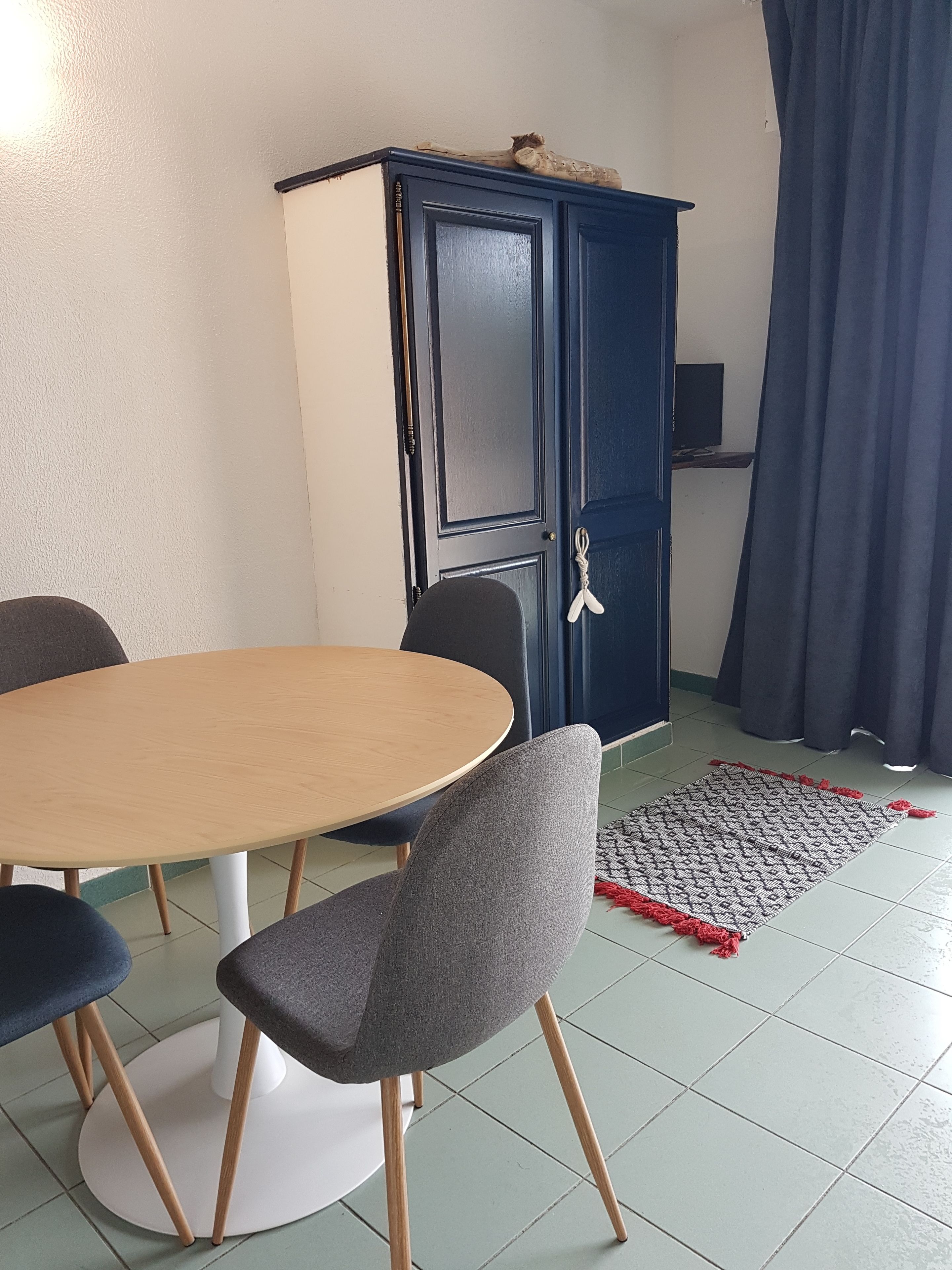 A dining area with a round table, four chairs, a dark blue cabinet, and a patterned rug.