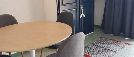 A dining area with a round table, four chairs, a dark blue cabinet, and a patterned rug.