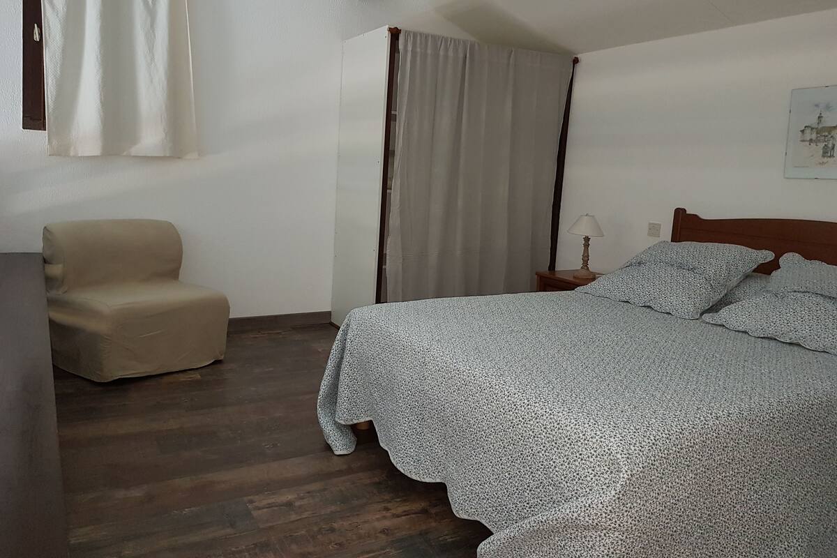 A bedroom with a bed, a chair, a nightstand, and a window with curtains.