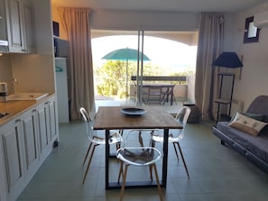 A dining area with a table and chairs, a kitchen area with cabinets, and a view of the outdoors. - résidence Costa D'oru (Saint-Florent)