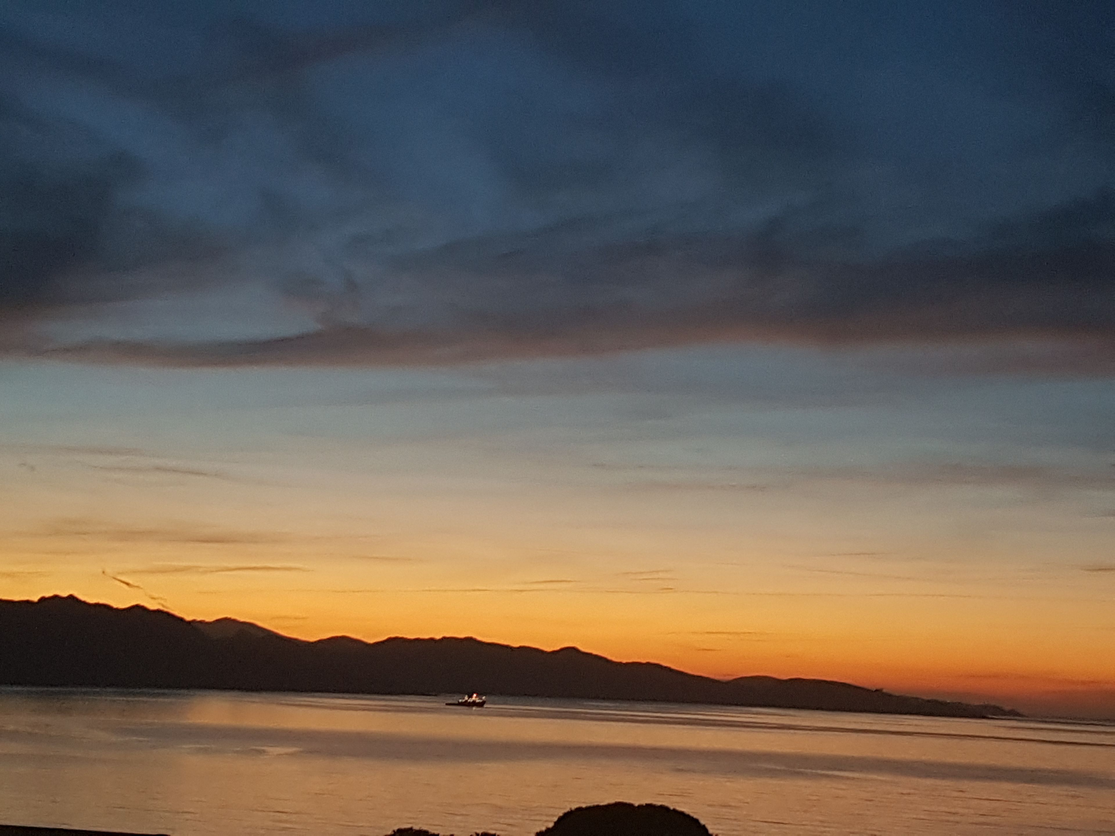 Um pôr do sol sobre águas calmas, com montanhas ao longe.