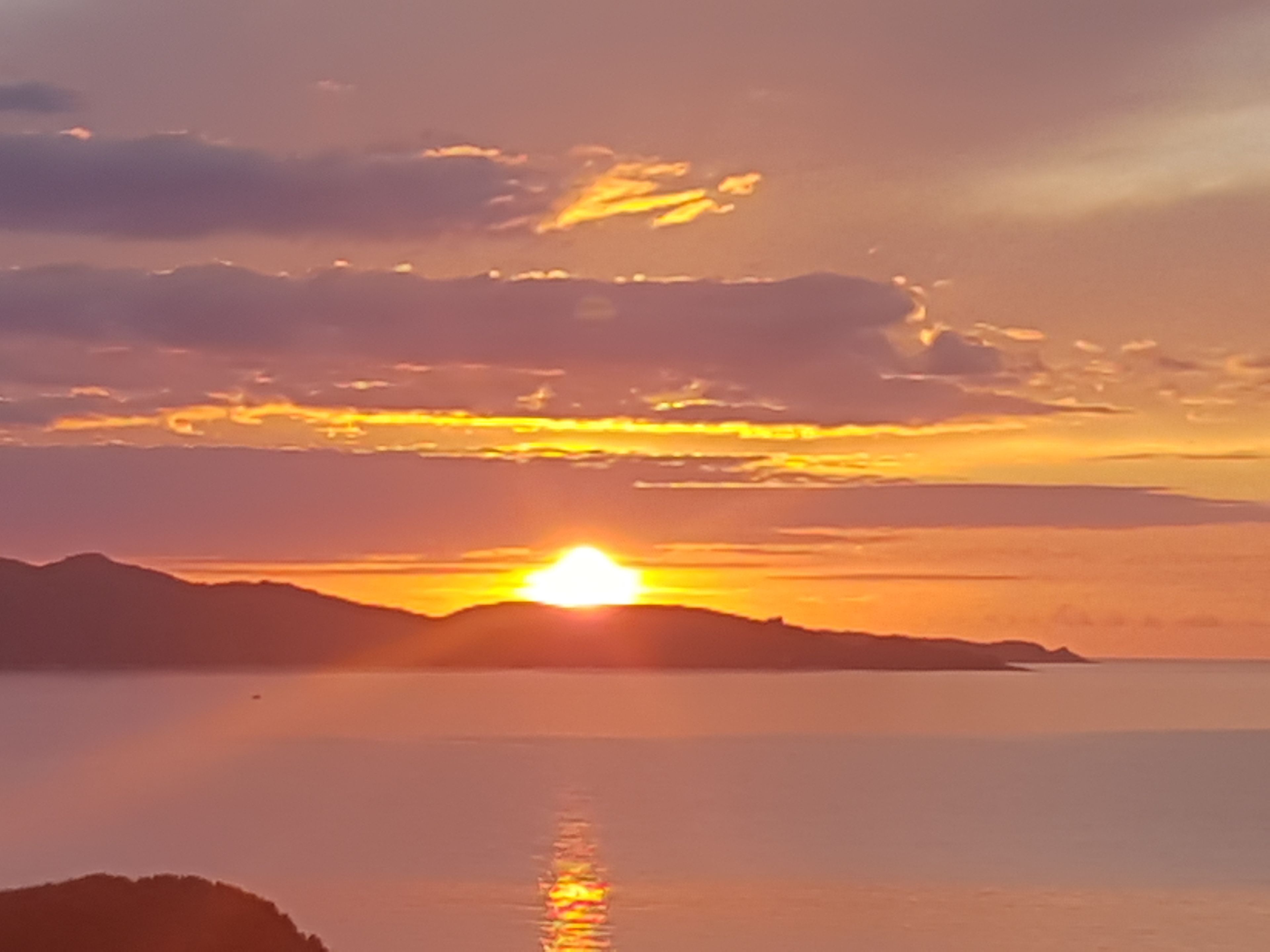 A sunset over a calm body of water with distant landforms.