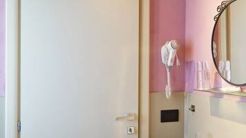 Un baño con un lavamanos blanco, un espejo, un secador de pelo y un cubo de basura.