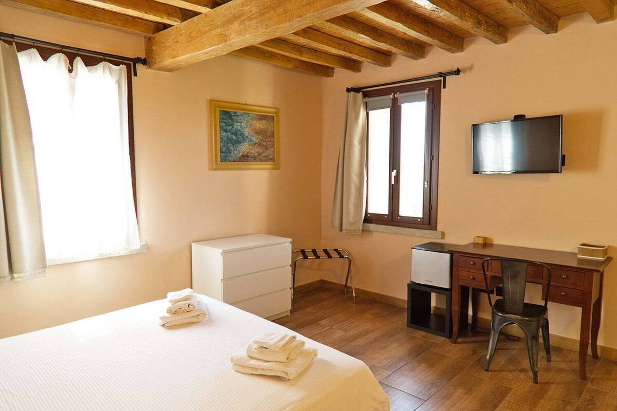 Een slaapkamer met een bed, een bureau, een stoel, een televisie en een raam met gordijnen.