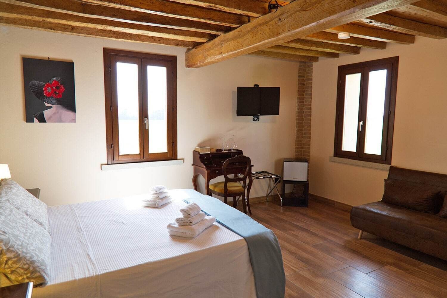 Quarto com cama, escrivaninha, cadeira, televisão e sofá.